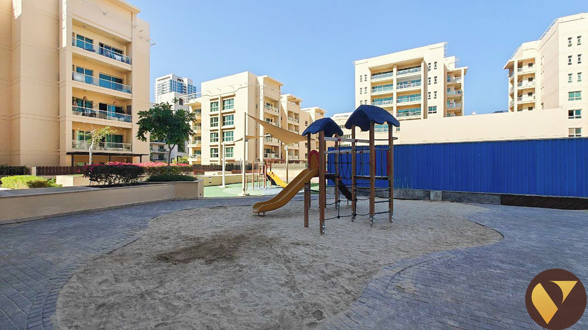 Un parque infantil con tobogán y estructuras para escalar, rodeado de edificios residenciales.
