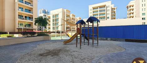 Un parque infantil con tobogán y estructuras para escalar, rodeado de edificios residenciales.