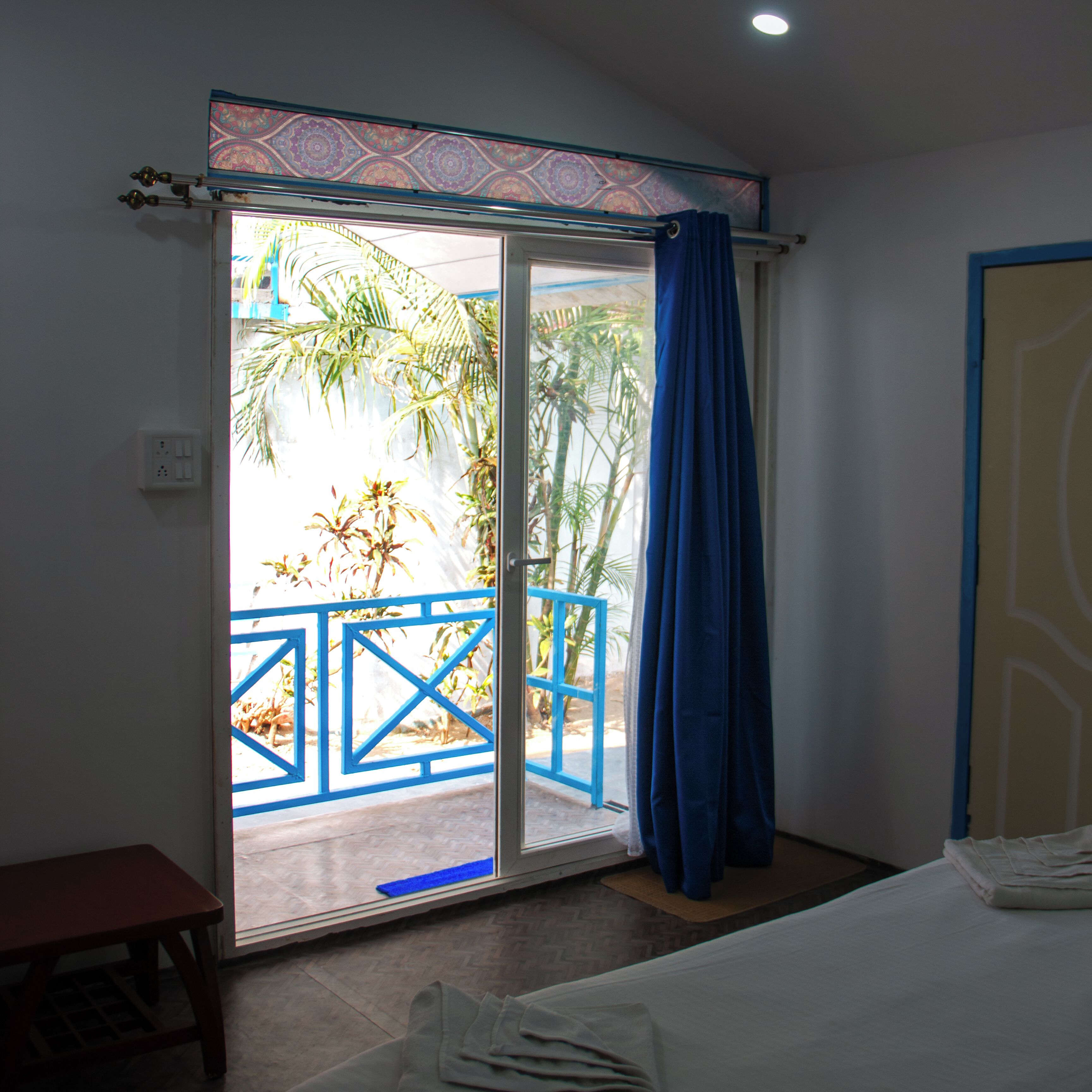 A room with a sliding glass door leading to a balcony with a blue railing and palm trees.