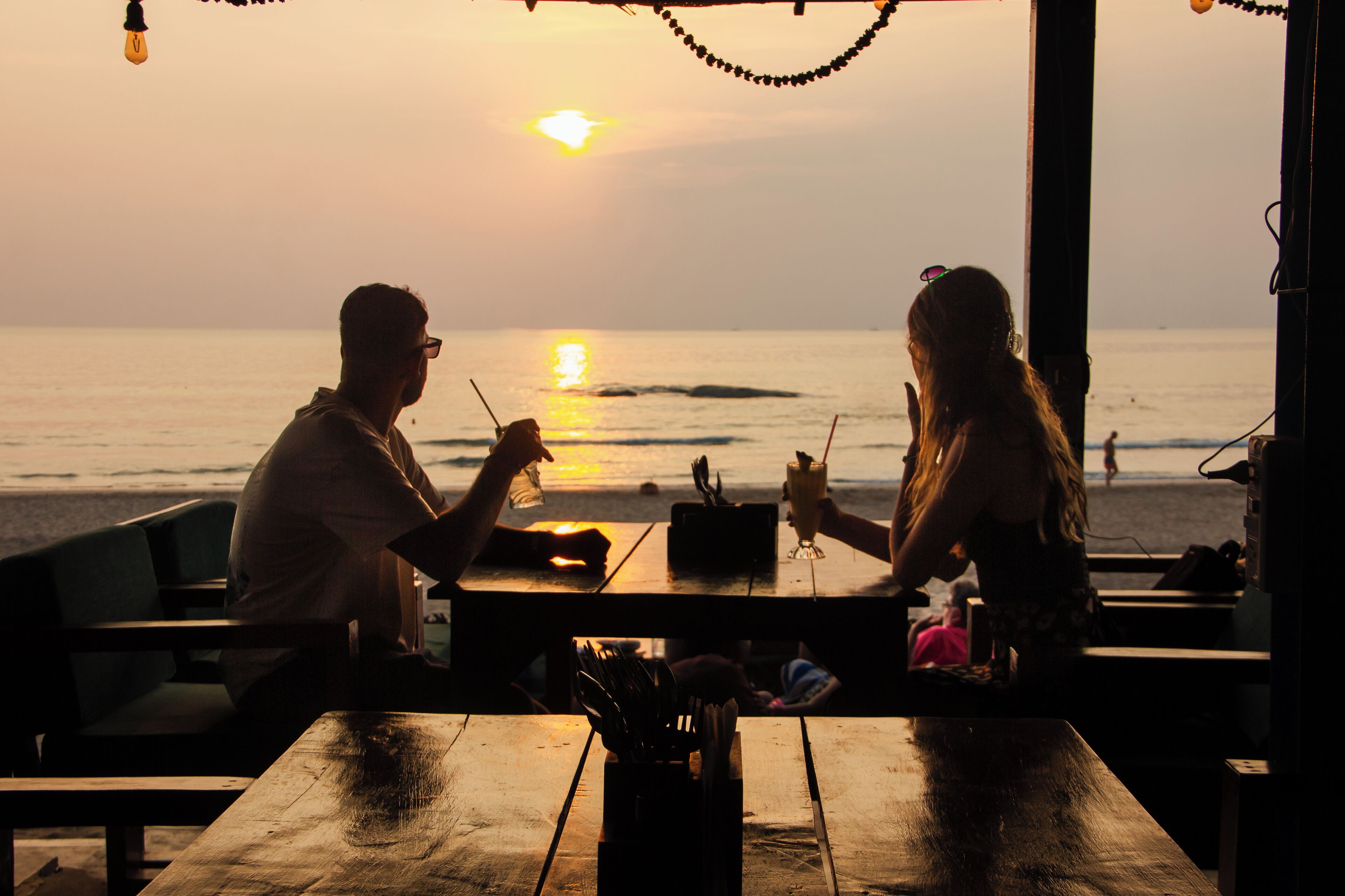 A sunset view from a beachside restaurant with wooden tables and chairs.