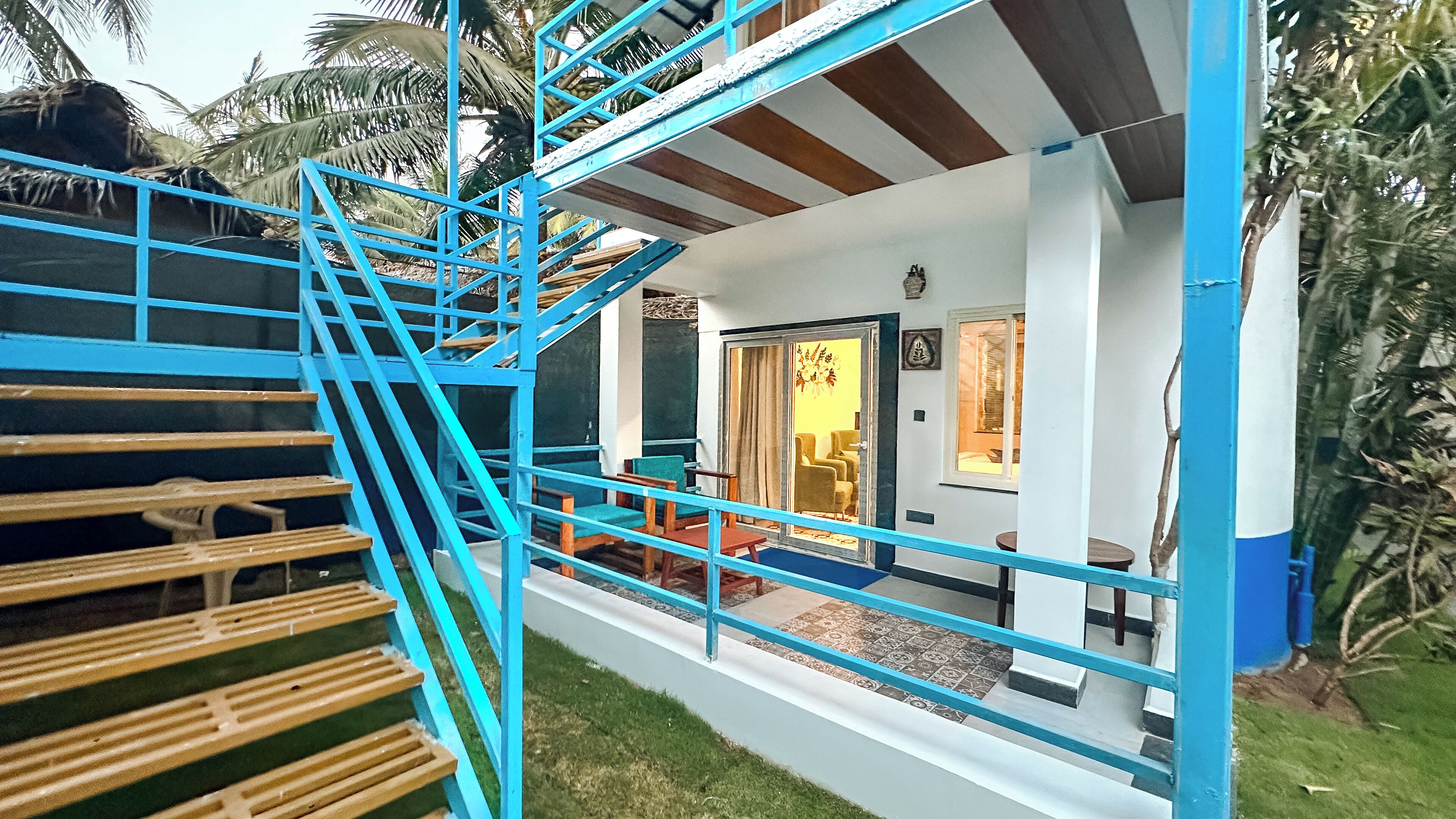Uma casa com vários andares, apresentando uma escada azul, uma porta que dá para um espaço com uma cadeira e uma mesa, e uma pequena varanda.