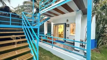 Uma casa com vários andares, apresentando uma escada azul, uma porta que dá para um espaço com uma cadeira e uma mesa, e uma pequena varanda.