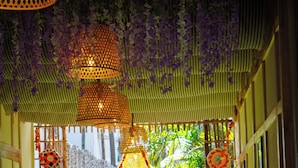A corridor with hanging purple flowers, patterned lanterns, and a bench. - New Common Home (Canacona)
