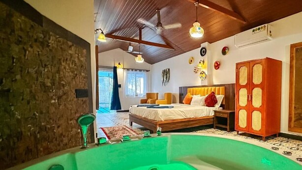 A room with a large green bathtub, a wooden ceiling, a bed with pillows, and a wardrobe. - New Common Home (Canacona)