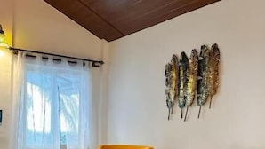 A room with two yellow armchairs, a patterned rug, a decorative wall hanging, and a ceiling fan. - New Common Home (Canacona)