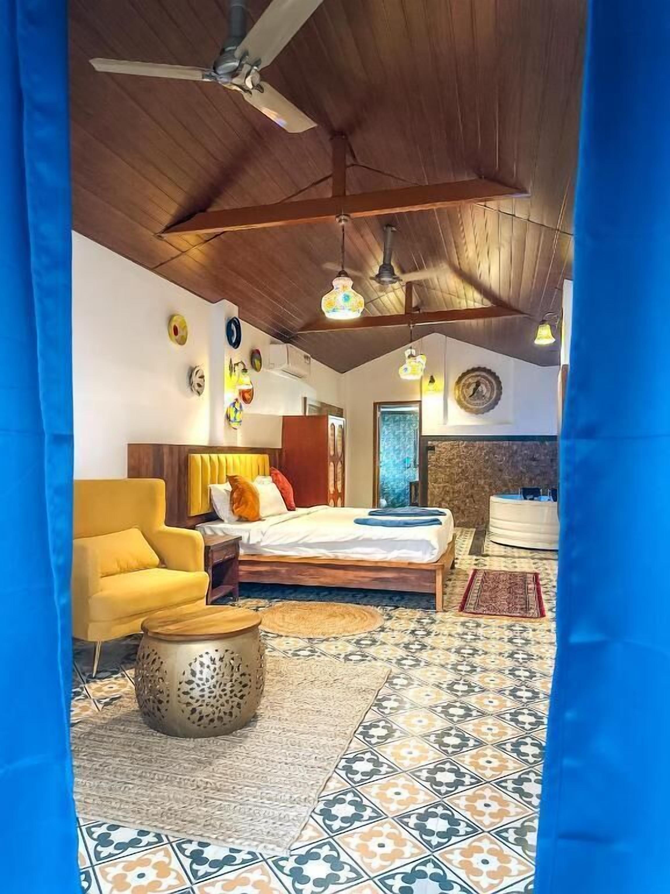 A bedroom with a bed, a yellow armchair, a round table, and patterned floor tiles.