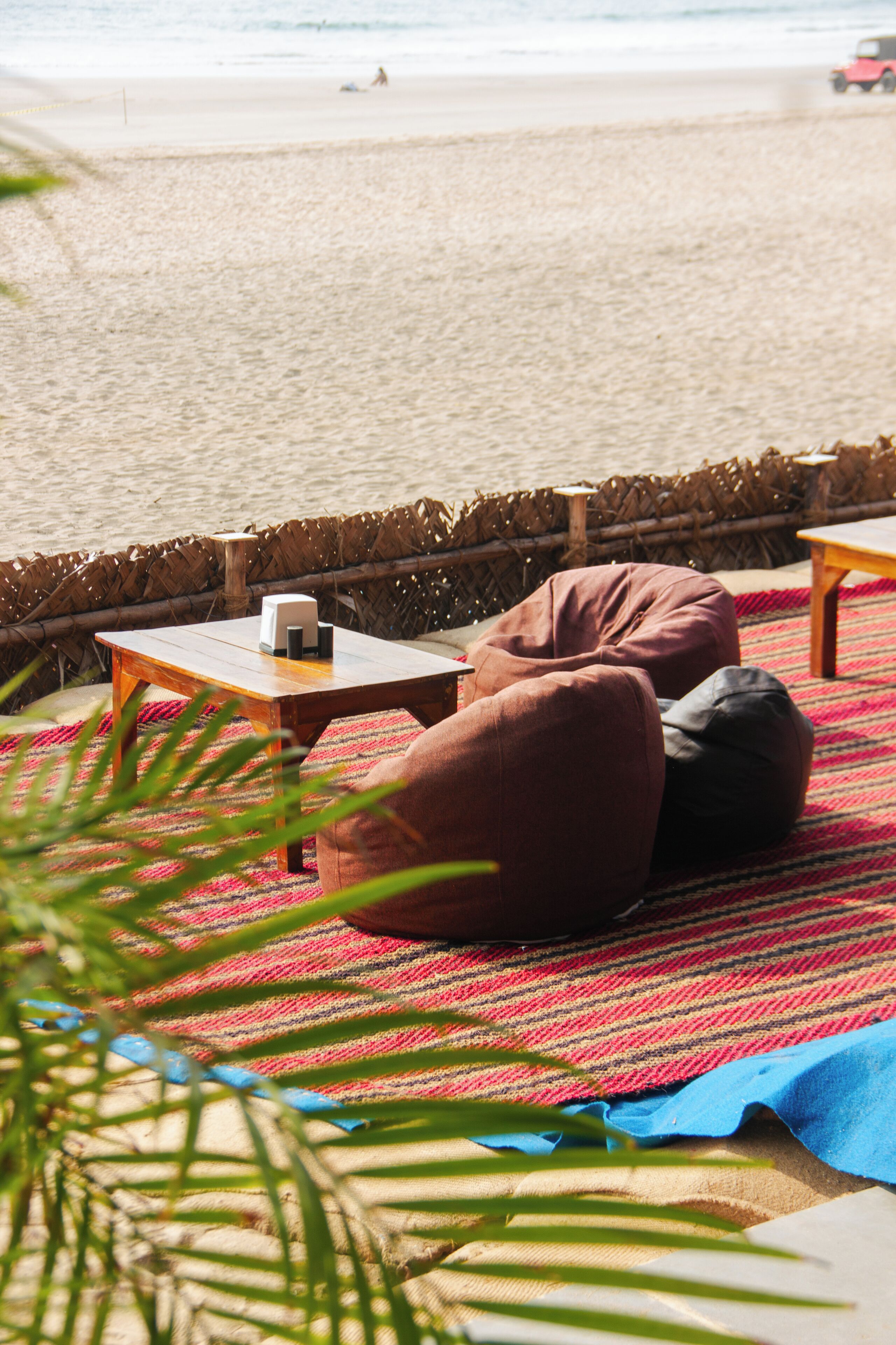 A beachside seating area with a table and two bean bags on a striped rug.