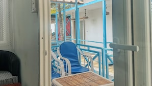A room with a wicker table, a blue chair, and a red stool. - New Common Home (Canacona)