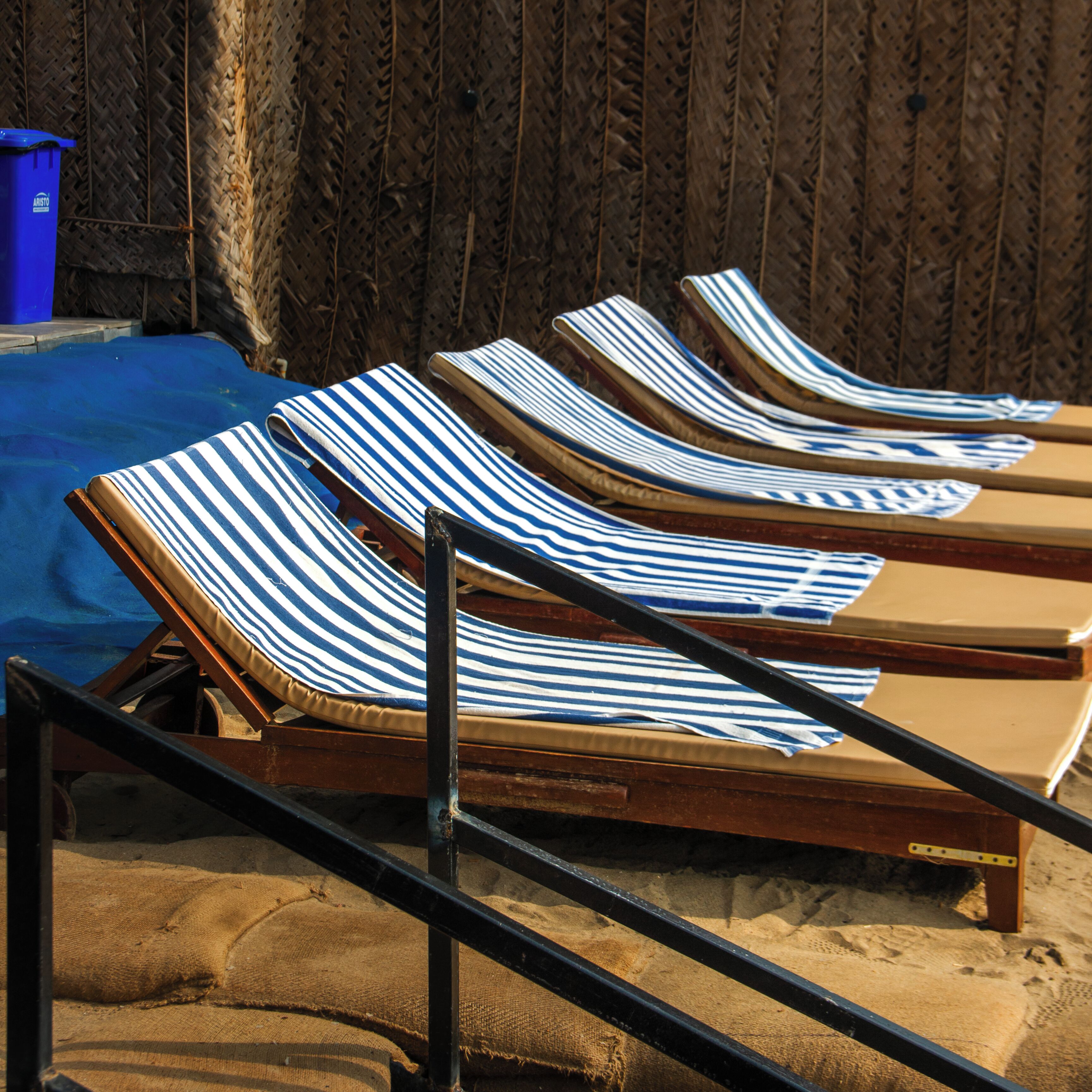 Sun loungers with striped towels, a blue trash bin, and a wooden fence in the background.