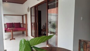 A room with a wooden bed, a glass door leading to a balcony, and a large green plant. - Hidden Point Villa 5 minutes to rice field walk. 1BD with Pool Walk to Ubud 

 (Bali)