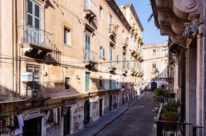 Una calle estrecha flanqueada por edificios, con balcones con barandillas y diversos detalles arquitectónicos.