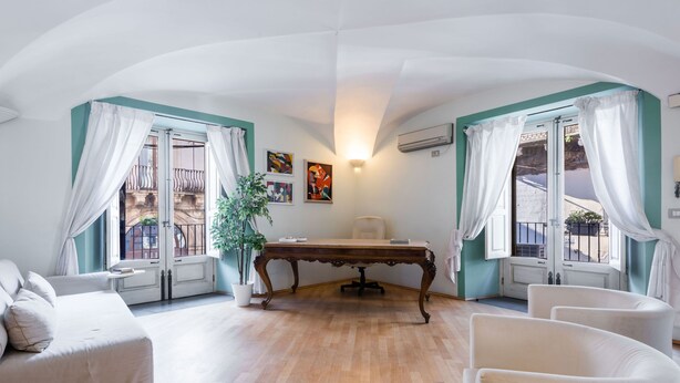 Une pièce avec un plancher en bois, un canapé blanc, une table en bois et des rideaux blancs.