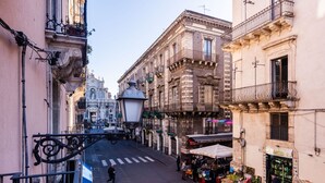 Une rue étroite bordée de bâtiments des deux côtés, un étal de marché proposant des produits frais, et une vue dégagée sur un bâtiment historique en arrière-plan.