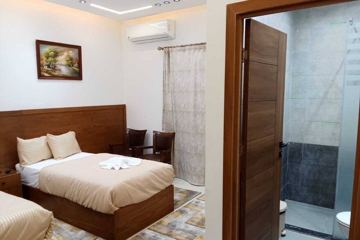 Une chambre d’hôtel avec un lit en bois, un petit bureau, une chaise, une douche et des toilettes.