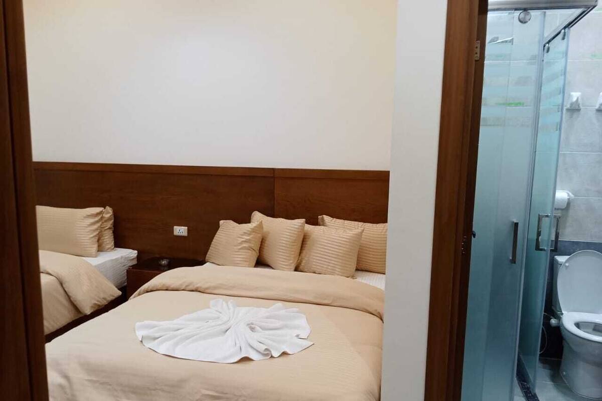 Une chambre d’hôtel avec deux lits, une tête de lit en bois et une cabine de douche en verre.
