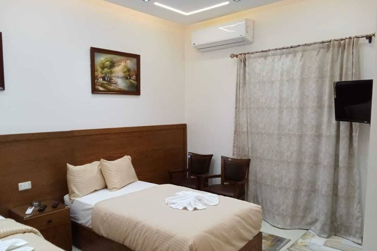 Une chambre d’hôtel avec un lit doté d’une tête de lit en bois, un téléviseur à écran plat, un tableau au mur et un rideau.