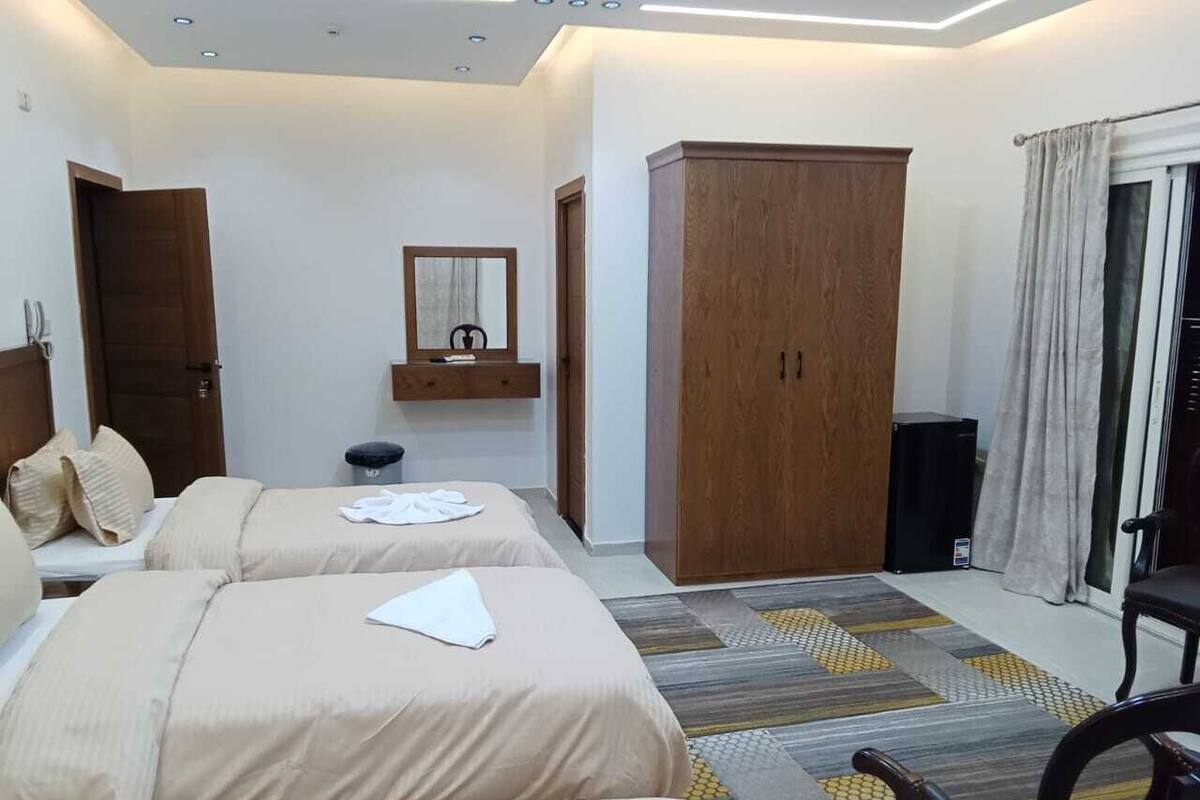 Une chambre d’hôtel avec deux lits, une armoire, un miroir et une fenêtre avec des rideaux.