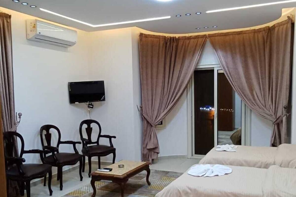 Une chambre d’hôtel équipée d’une télévision, de quatre chaises en bois, d’une petite table et de deux lits avec des serviettes.