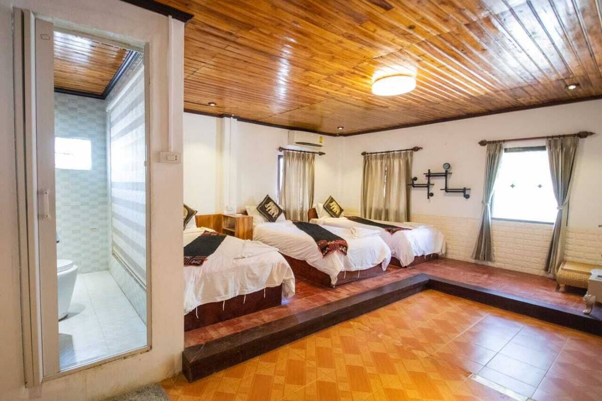 Habitación de hotel con tres camas, techo de madera, piso de baldosas y vista al exterior.