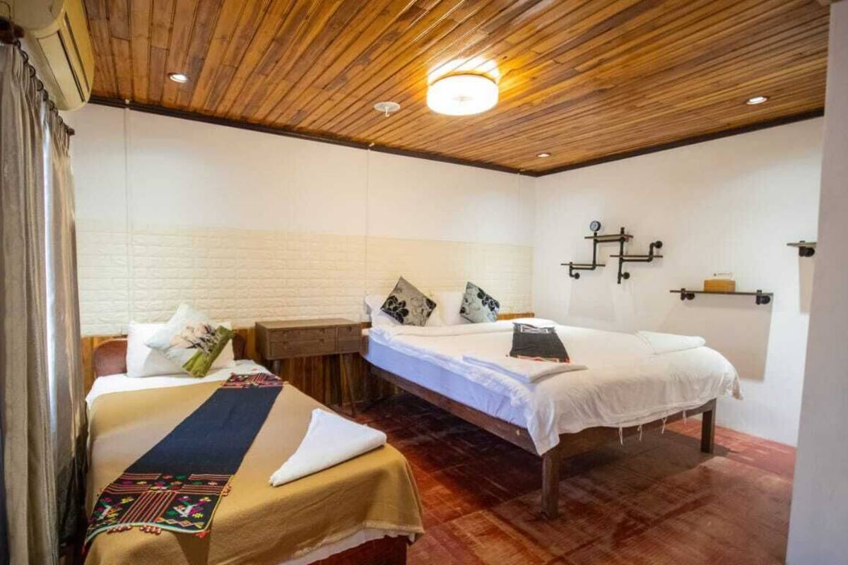 Un dormitorio con dos camas, techo de madera y pared de ladrillo blanco.