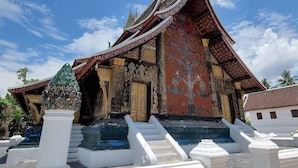 Un templo tradicional con arquitectura ornamentada, una escalera que conduce a la entrada y un cielo azul brillante.