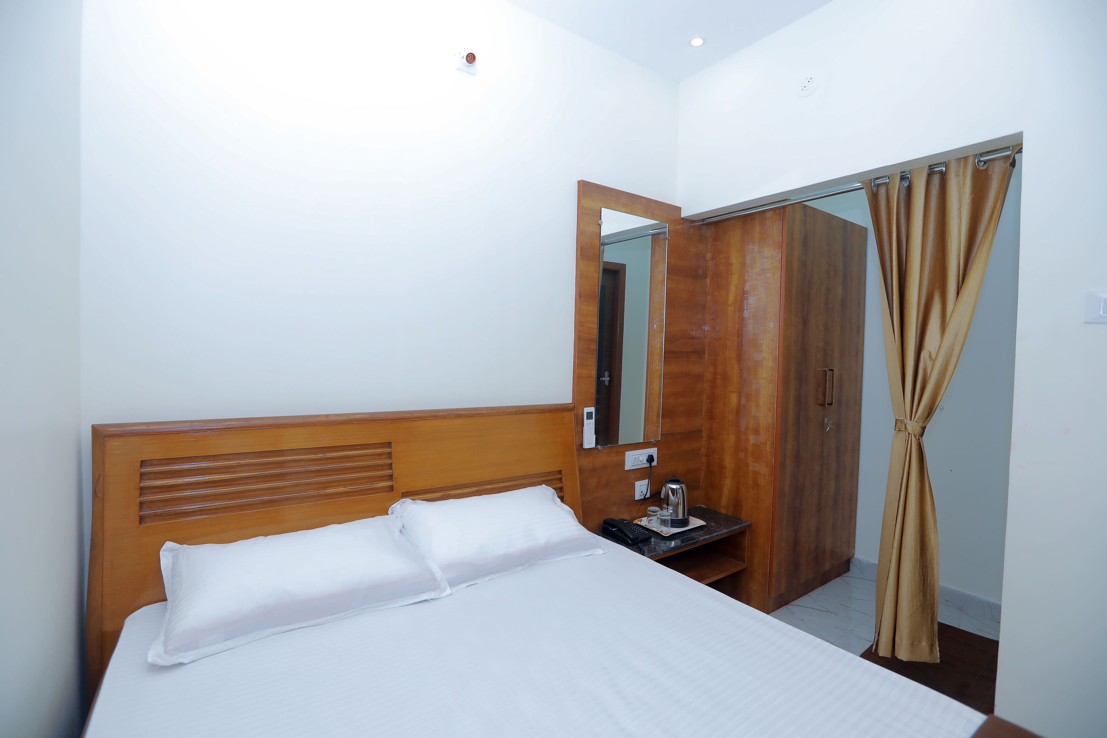 Ein Hotelzimmer mit einem hölzernen Kopfteil, einem Bett mit weißer Bettwäsche, einem Nachttisch mit Wasserkocher und einem Spiegel an der Wand.