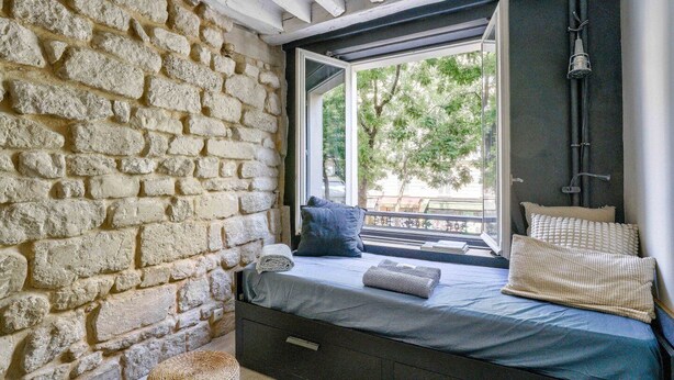 Une pièce chaleureuse avec un mur en pierre, un lit offrant une belle vue et une fenêtre donnant sur les arbres.