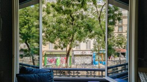 Une pièce avec une grande fenêtre donnant sur la rue, un canapé bleu et un livre posé sur le rebord de la fenêtre.