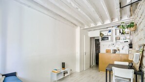 Un espace de vie compact comprenant un lit, un petit bureau, une chaise et un coin cuisine.