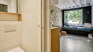 Une chambre moderne avec un mur en pierre, une grande fenêtre et un lit avec des oreillers.