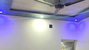 Ein Hotelzimmer mit Bett, grünem Kopfteil, weißen Kissen, einer roten Decke, einem Deckenventilator und einem blauen Mülleimer.