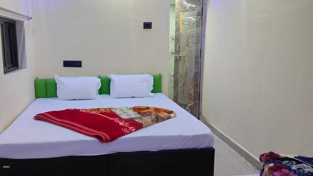 Ein schmales Hotelzimmer mit einem Einzelbett, weißer Bettwäsche, einem grünen Kopfteil und einer roten Decke.