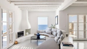 A modern living room with a sofa, a coffee table, and a bookshelf. - Villa Oleandri Mykonos (Mykonos)