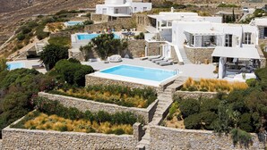 A modern villa with a swimming pool, stone walls, and a view of the surrounding landscape. - Villa Oleandri Mykonos (Mykonos)