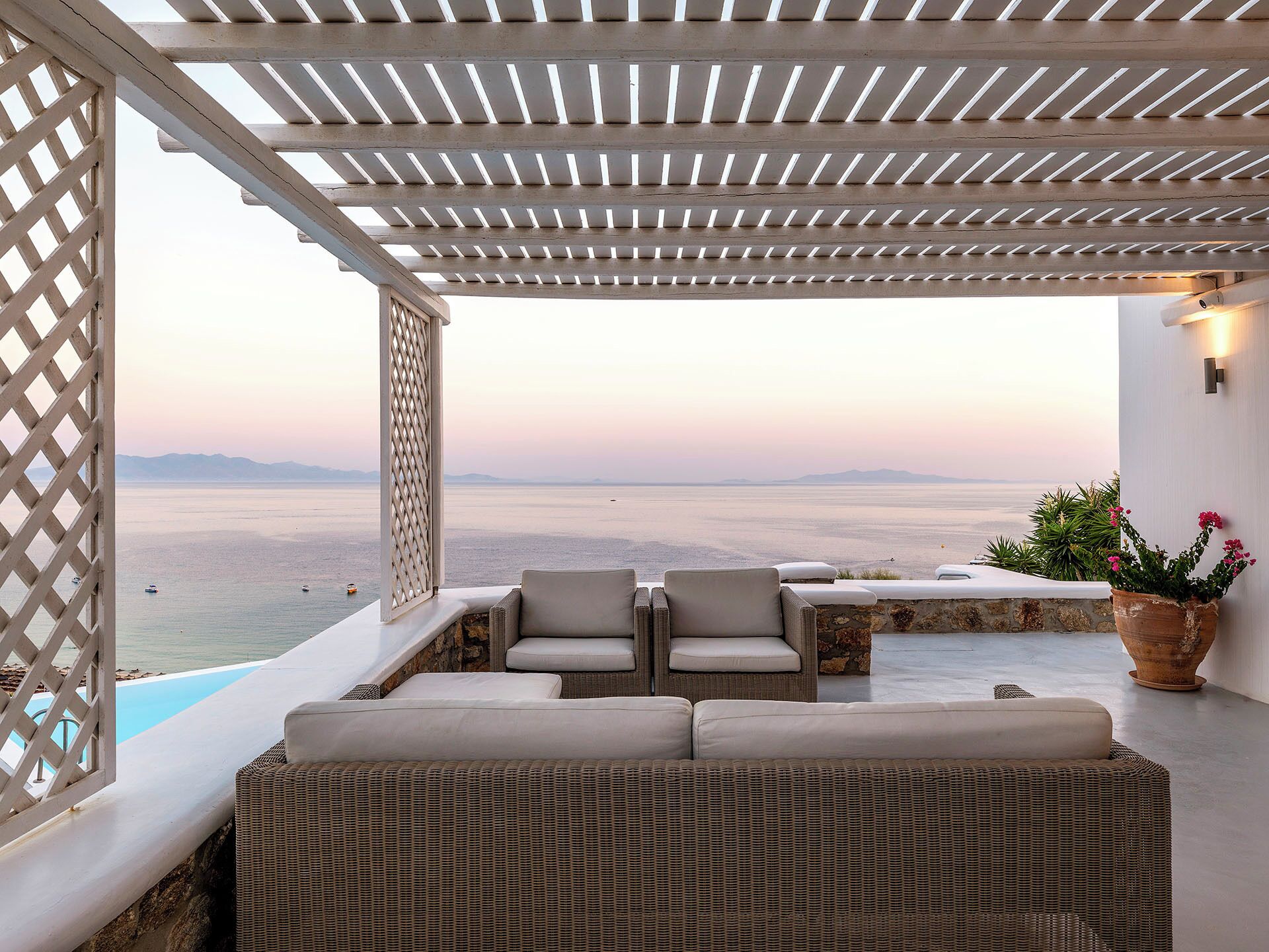 A covered outdoor seating area with a view of the sea, a stone wall, and a potted plant.
