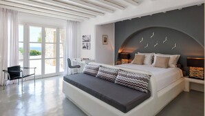 A modern bedroom with a large bed, a desk, and a view through the glass doors. - Villa Oleandri Mykonos (Mykonos)