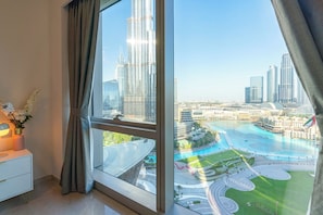 A modern hotel room with a large window offering a view of a cityscape and a waterfront promenade. - Full Burj Khalifa & Fountain View | All Rooms (Dubai)