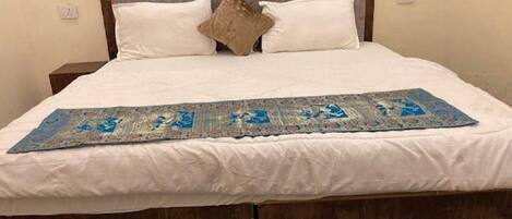 A bed with white linens, a brown headboard, and a decorative blue and gold runner.