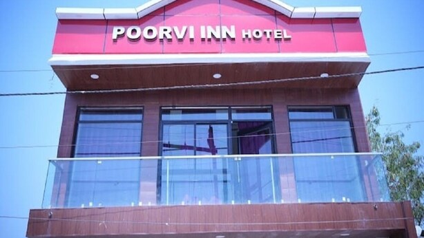 L’extérieur de l’hôtel Poorvi Inn se distingue par une enseigne bien visible, de grandes fenêtres et un balcon doté d’une balustrade en verre.