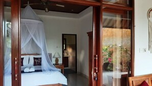 A bedroom with a bed, a nightstand, a lamp, and a window with a view of greenery. - Private One BD with Pool Overlooking to Rice Fields By Hidden Point Villa

 (Bali)