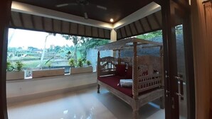 A four-poster bed with a red bedspread in a room with a view of a garden. - Private One BD with Pool Overlooking to Rice Fields By Hidden Point Villa

 (Bali)