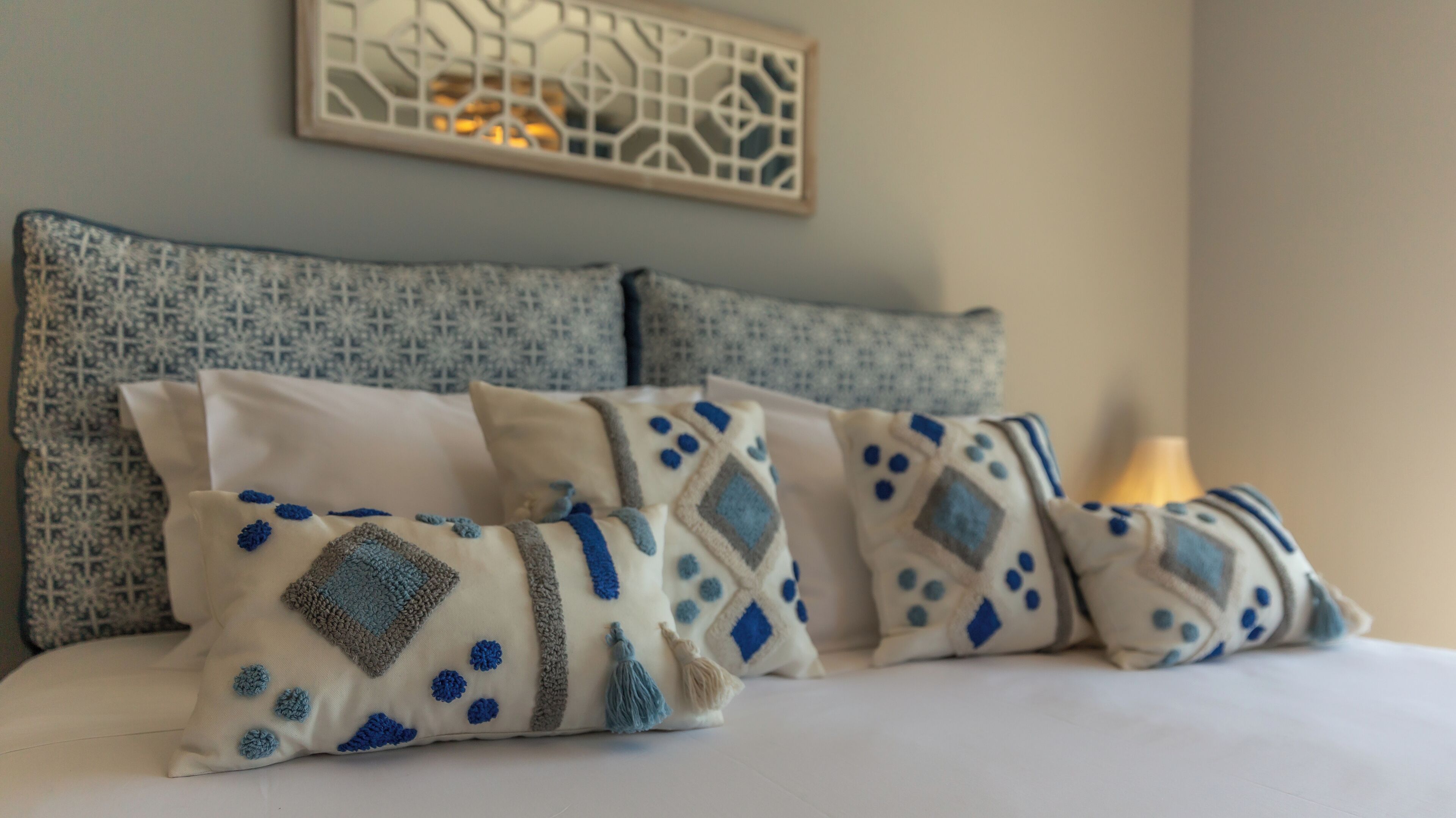 A bed with four decorative pillows, a wall-mounted artwork, and a bedside lamp.