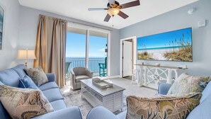 Un salon moderne avec un canapé bleu, une table basse et un grand tableau représentant une scène de plage.