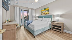 A bedroom with a bed, nightstands, a ceiling fan, a painting, and a view of the outside. - Legacy Tower I Unit 302 | Overlooking the Beautiful Gulf! (Gulfport)