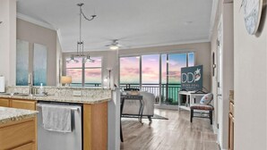 A spacious kitchen with granite countertops, a central island, and a view of the sunset through large windows. - Legacy Tower I Unit 302 | Overlooking the Beautiful Gulf! (Gulfport)