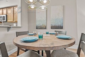 Un espace repas avec une table ronde en bois, des assiettes et des verres bleus, le tout entouré de chaises.
