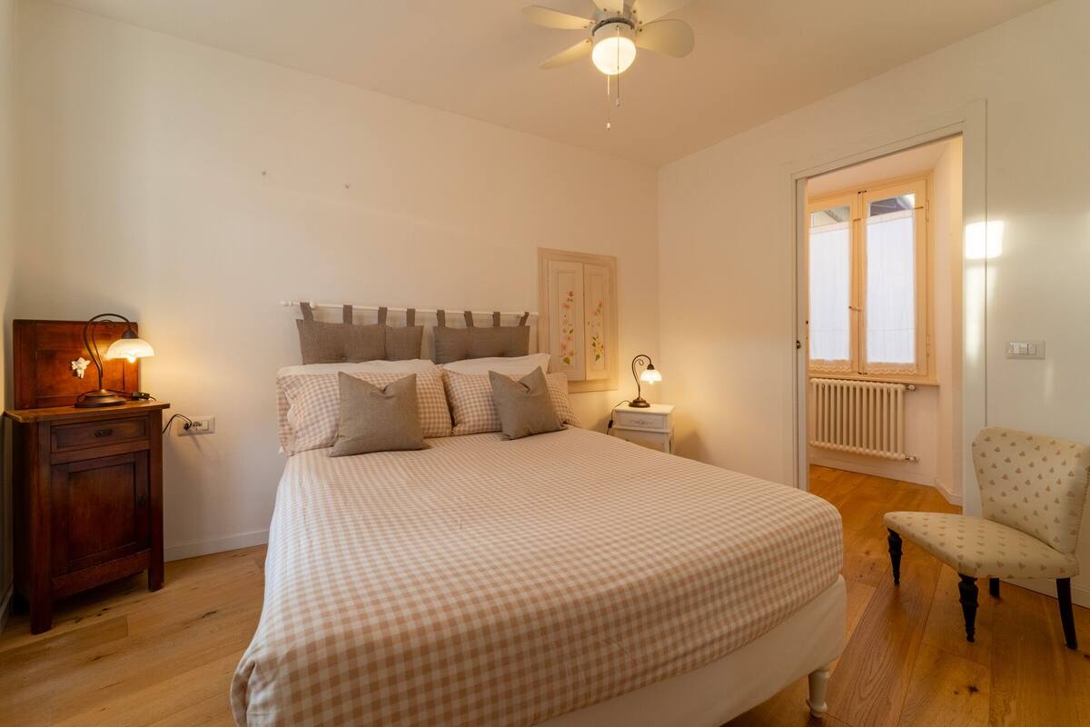 Een slaapkamer met een bed, nachtkastjes, een stoel, een plafondventilator en een raam met uitzicht.