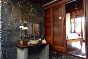 A bathroom with a stone wall, a wooden door, a sink with a mirror, and a potted plant. - Hidden Point Villa 5 minutes to rice field walk.  Wooden House with Large Pool 
 (Bali)