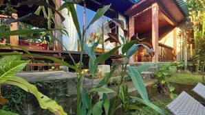 Um jardim tropical com muro de pedra, deck de madeira e área de estar coberta.