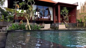 Uma área junto à piscina com um deque de madeira, espreguiçadeiras e uma casa com janelas amplas e telhado vermelho.